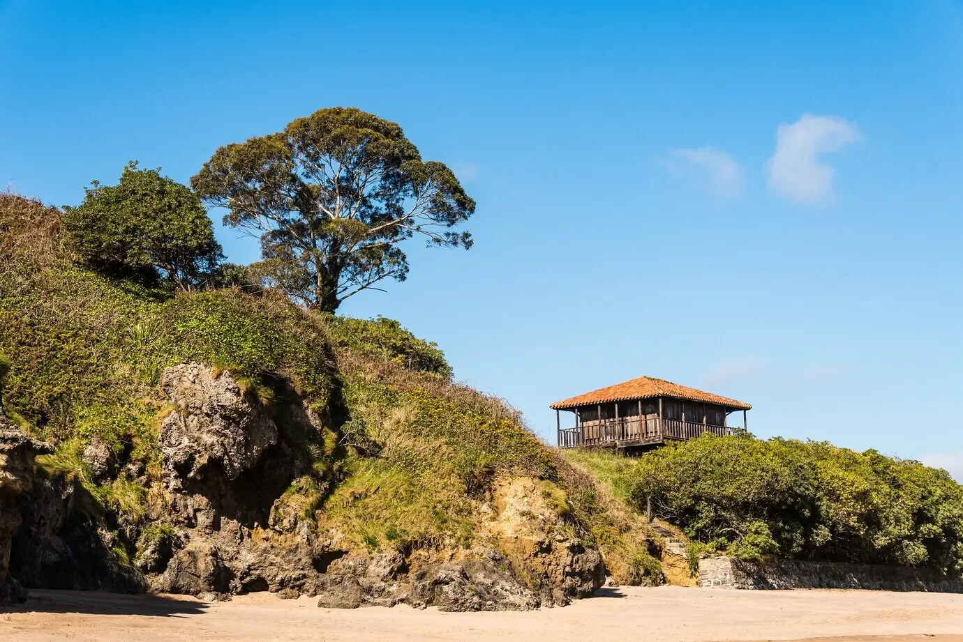 Schöne Aussicht auf ein altes Haus in Strandnähe, umgeben von Bäumen und Gras, unter einem blauen Himmel.
